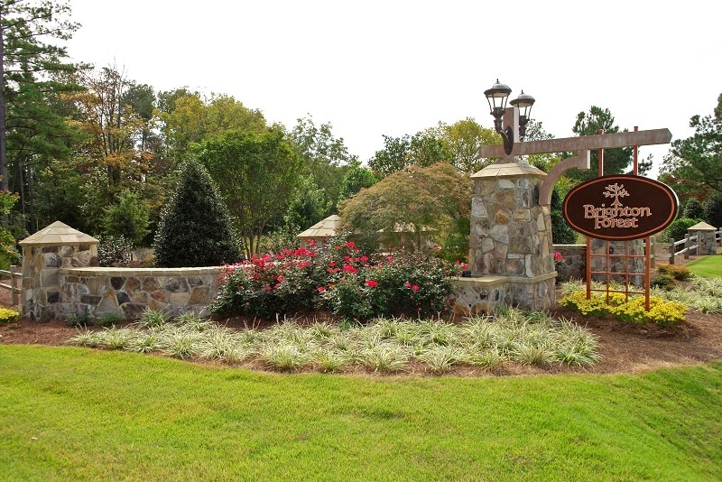 Brighton Forest entrance sign surrounded by stonework, trees, and landscaping